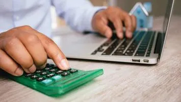 Hands typing on a calculator and laptop